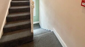 Eine Treppe mit Teppichstufen, einem weißen Geländer und einer roten Steckdose an der Wand.