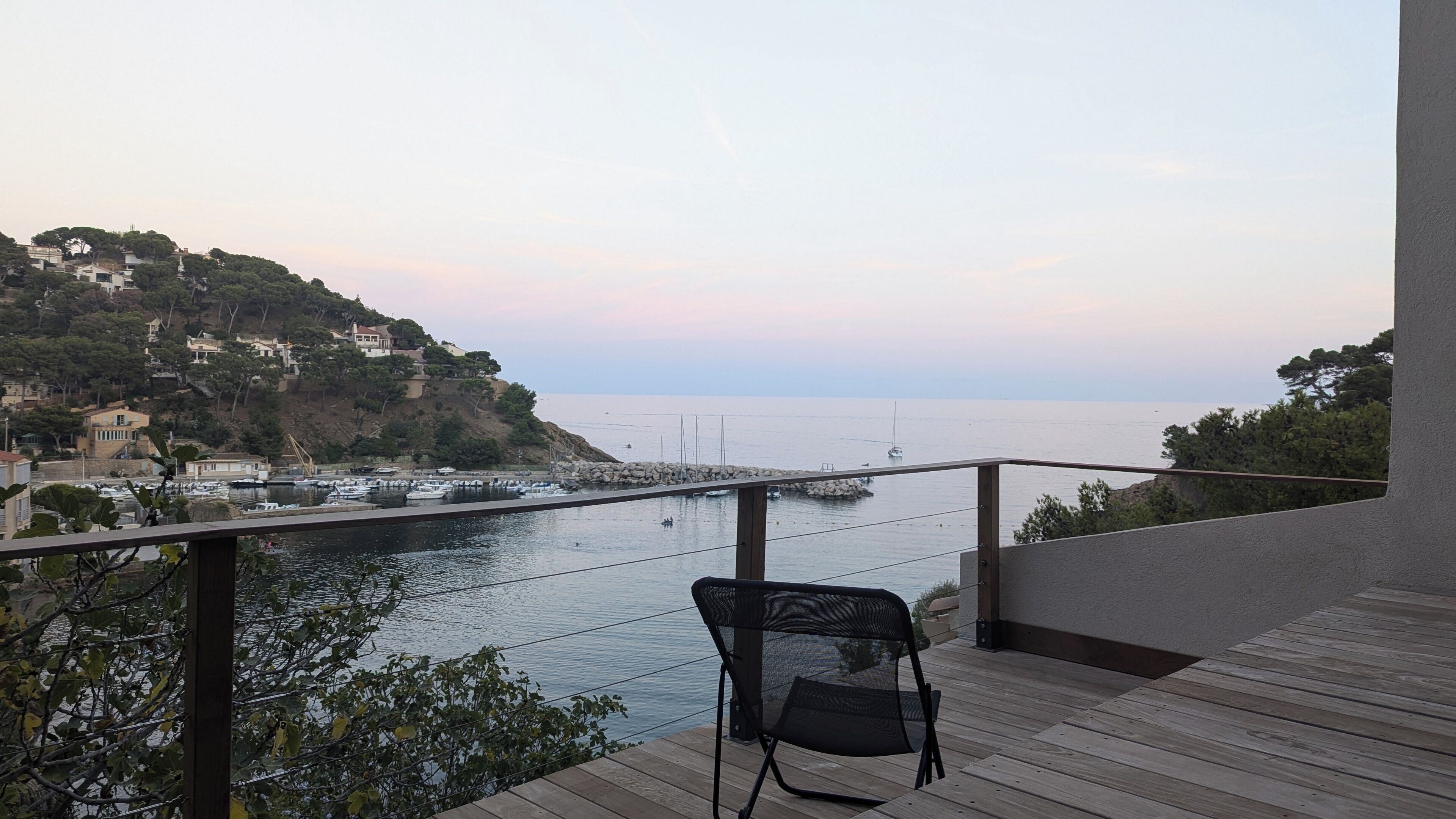 A balcony with a chair overlooking a marina and a coastal town.