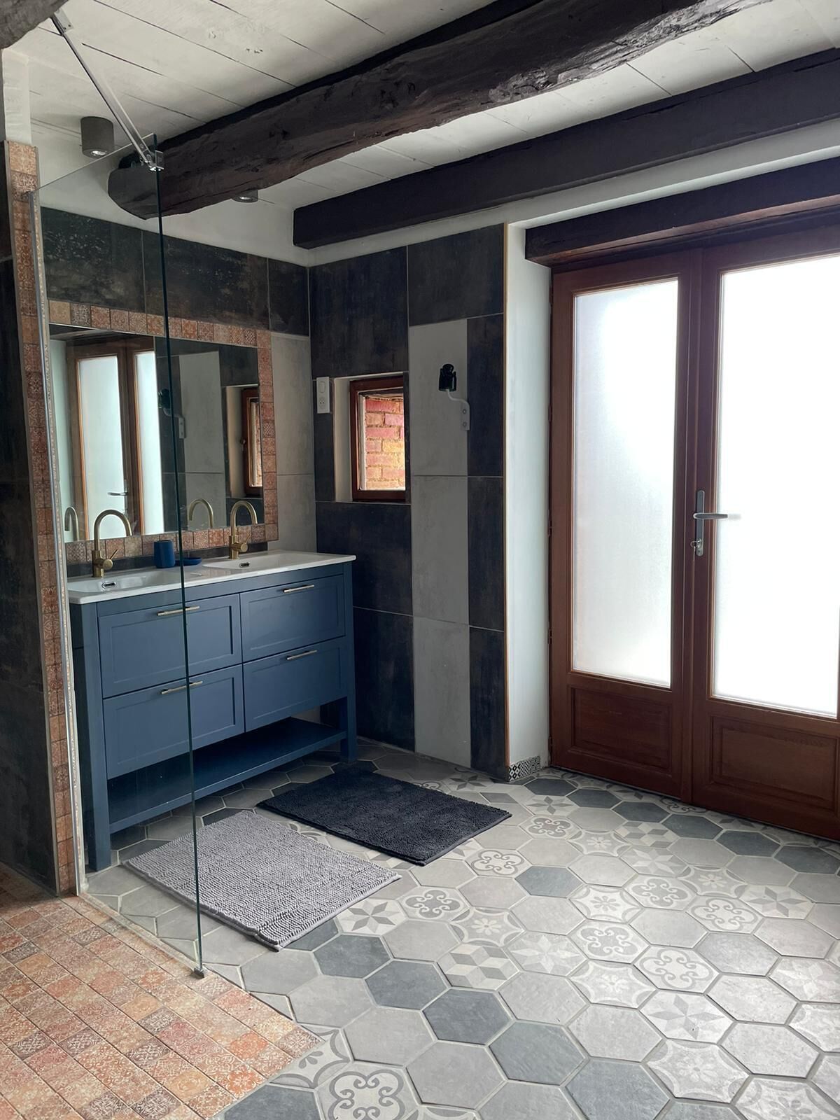 A bathroom with a blue vanity, a large mirror, a window, and a door with frosted glass panels.