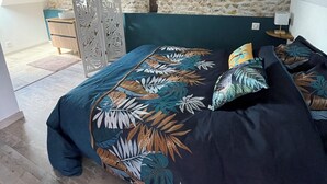 A bedroom with a sloped ceiling, stone wall, and a bed with a tropical leaf pattern bedspread. - Gite "Le Chatel (Prissac)