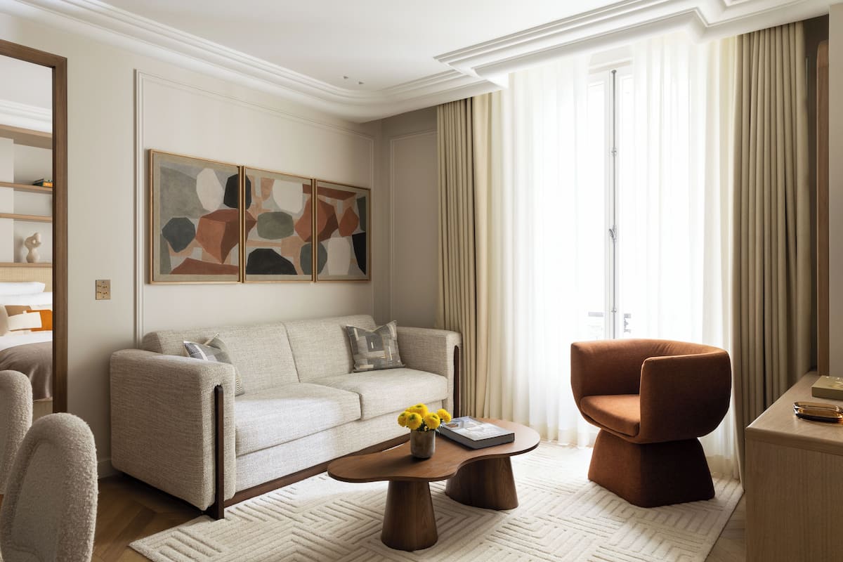 A modern living room with a beige sofa, a brown armchair, and a coffee table with a vase of yellow flowers.