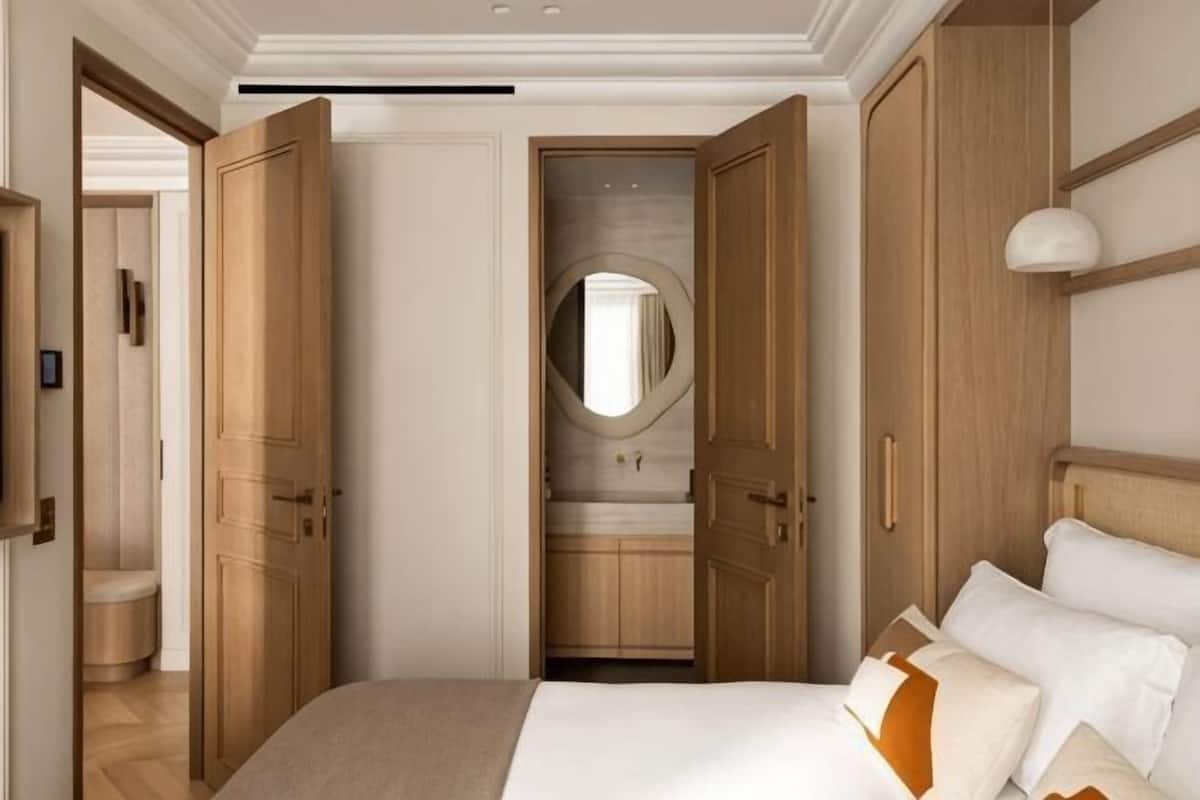 A bedroom with a large bed, wooden wardrobe, and a mirror.