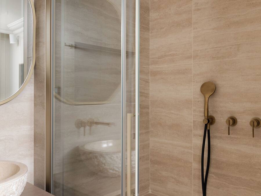 A modern bathroom with a glass-enclosed shower, a round mirror, and a beige-tiled wall.