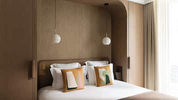Cama bem arrumada com duas almofadas, cabeceira de madeira e duas luminárias pendentes.
