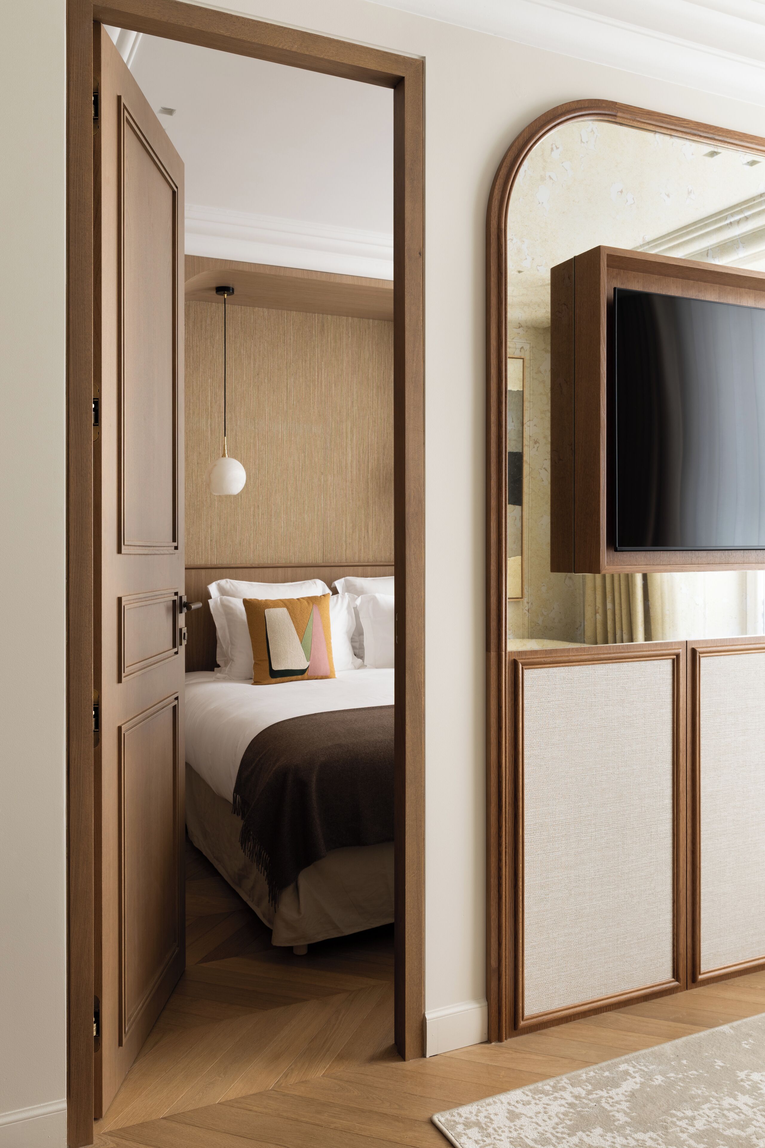 A hotel room with a wooden wardrobe, a bed with pillows, a hanging light fixture, and a television on a cabinet.