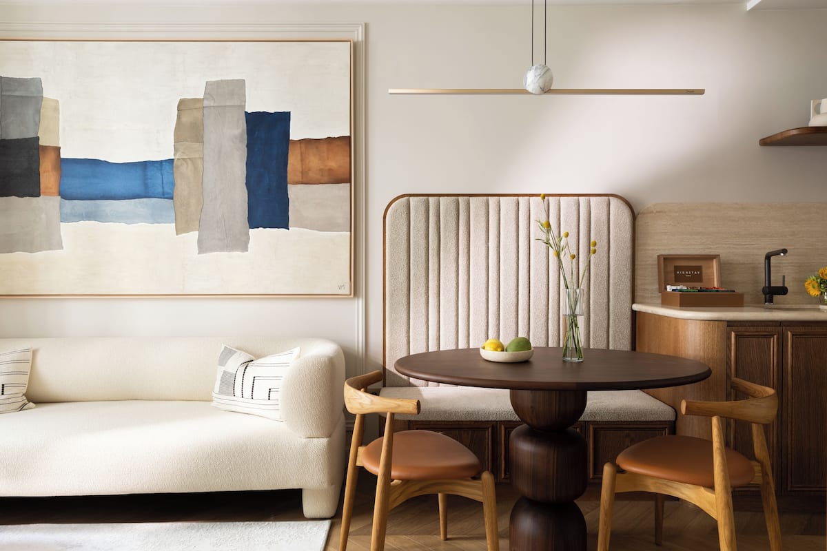 A modern living room with a sofa, a round table, and a chair. There is a painting on the wall and a ceiling light fixture.