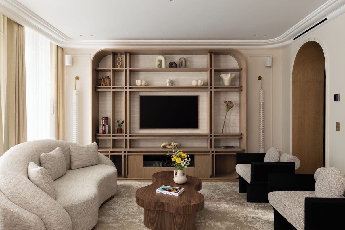 A modern living room with a large flat-screen TV, a beige sofa, a coffee table with a book, and a wooden console table with decorative items.