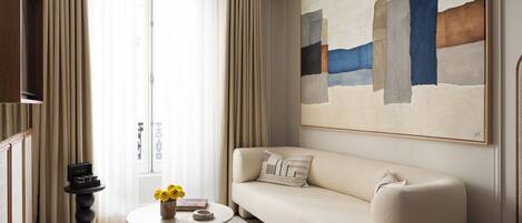 A modern living room with a beige sofa, a round coffee table with a vase of yellow flowers, and a large abstract painting on the wall.