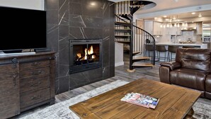 Un salon moderne doté d’une cheminée, d’un téléviseur, d’un canapé en cuir et d’un escalier en colimaçon menant à un niveau supérieur.