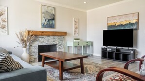 Un salon avec une cheminée en pierre, un téléviseur à écran plat, une table basse et un tapis à motifs.