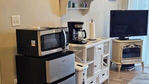 A compact kitchen with a refrigerator, microwave, coffee maker, and a television on a stand.