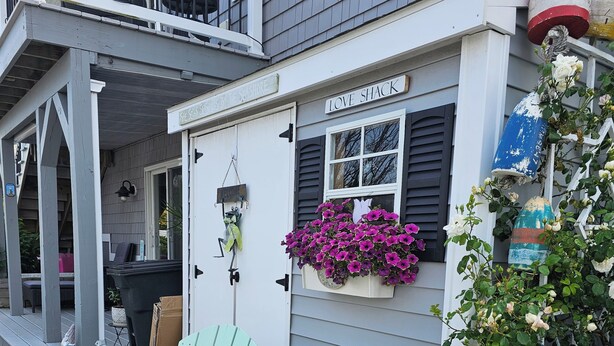 A quaint cottage with a porch, a green chair, and various potted plants.