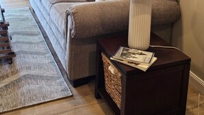 A living room with a sofa, two lamps, a framed photo collage, and a small table with magazines.