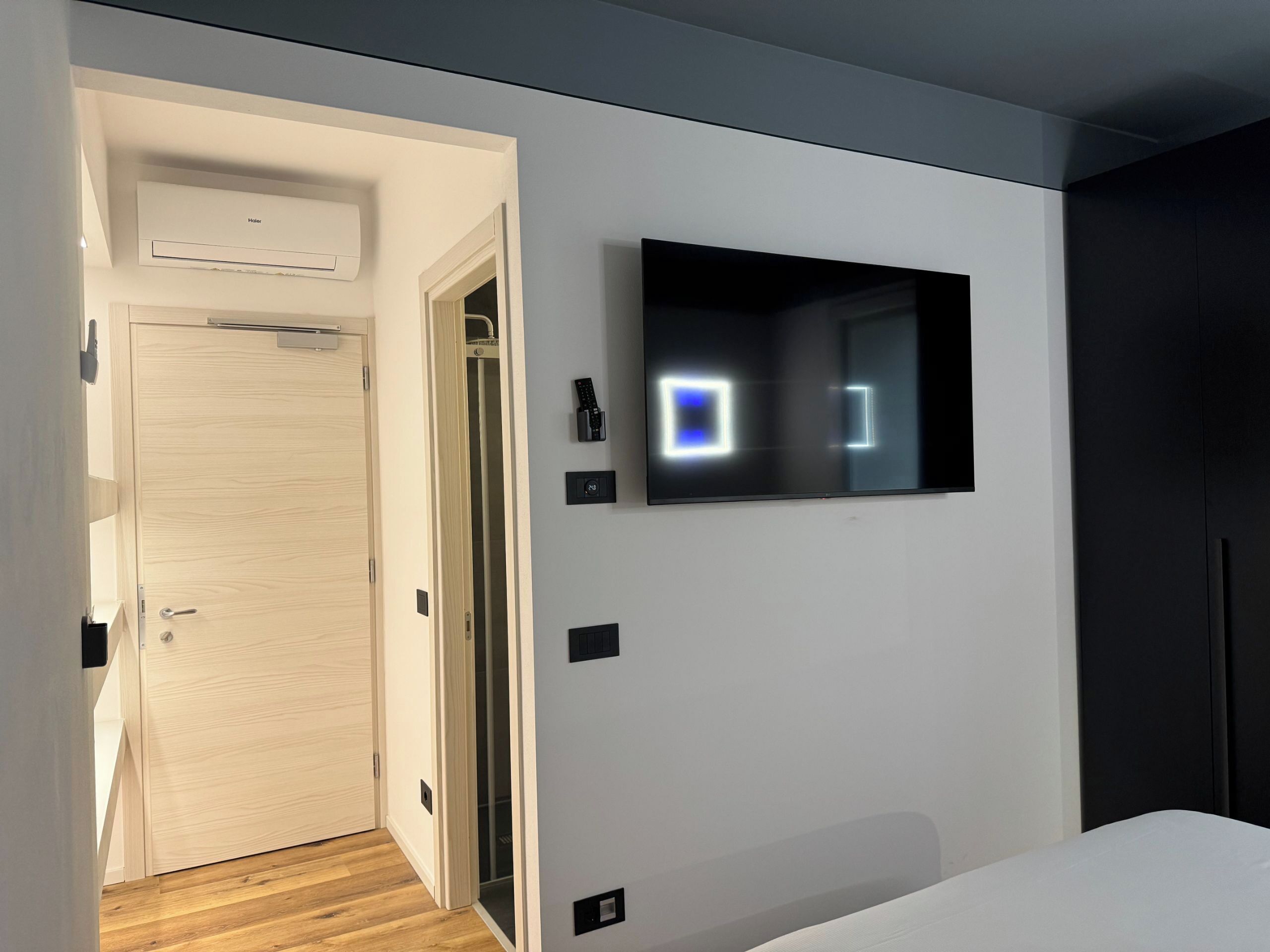 Een moderne hotelkamer met een houten deur, een wandgemonteerde televisie en een kledingkast.