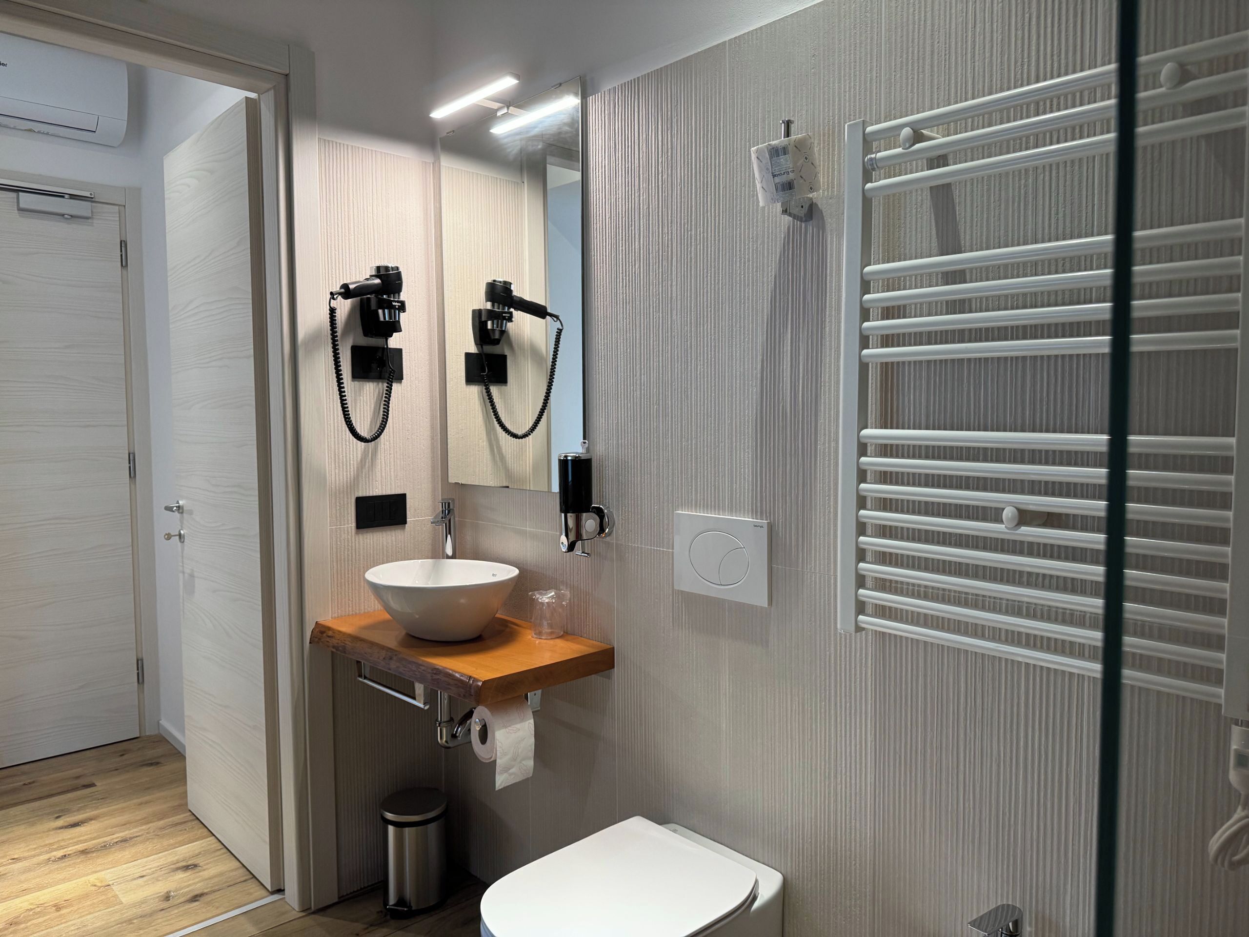 A modern bathroom with a wooden vanity, a white sink, a mirror, a towel rack, and a toilet.