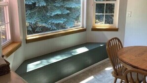 A room with a built-in bench under a large window, a dining table with chairs, and a small window with blinds.