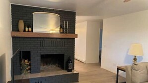 A living room with a fireplace, wooden flooring, a sofa, and a lamp.