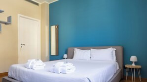 Ein ordentlich bezogenes Bett mit weißen Bettwäsche und Handtüchern, ein Nachttisch mit Lampe und eine Tür mit Griff.