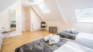 A bedroom with two beds, a radiator, a window, and a mirror. - Stewards Cottage - North East Escapes (Bamburgh)