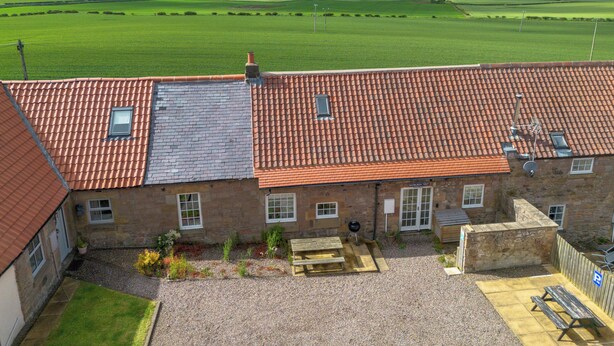 A building with a red-tiled roof, a gravel courtyard, and a view of a green field. - Stewards Cottage - North East Escapes (Bamburgh)
