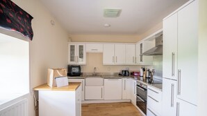 A compact kitchen with white cabinets, a microwave, a coffee maker, and a stove. - Stewards Cottage - North East Escapes (Bamburgh)