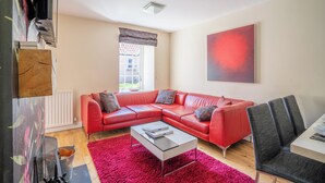 A modern living room with a red leather sofa, a white coffee table, and a large abstract painting on the wall. - Stewards Cottage - North East Escapes (Bamburgh)