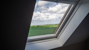 A skylight with a view of a green field and a cloudy sky. - Stewards Cottage - North East Escapes (Bamburgh)
