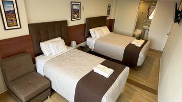 Habitación de hotel con dos camas, una silla y baño visible a través de una puerta abierta.