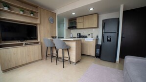 A modern kitchen with wooden cabinets, a built-in TV, a refrigerator, and two bar stools. - Increible Apartamento con vista cerca Provenza by Hoost 2510 (Medellín)