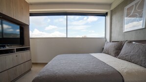 A bedroom with a large bed, a TV on a wooden cabinet, and a window with a city view. - Increible Apartamento con vista cerca Provenza by Hoost 2510 (Medellín)