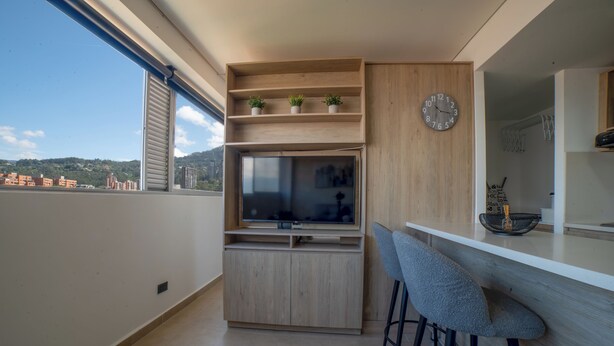 A modern kitchen with a built-in TV, wooden shelves, and a bar area with stools. - Increible Apartamento con vista cerca Provenza by Hoost 2510 (Medellín)
