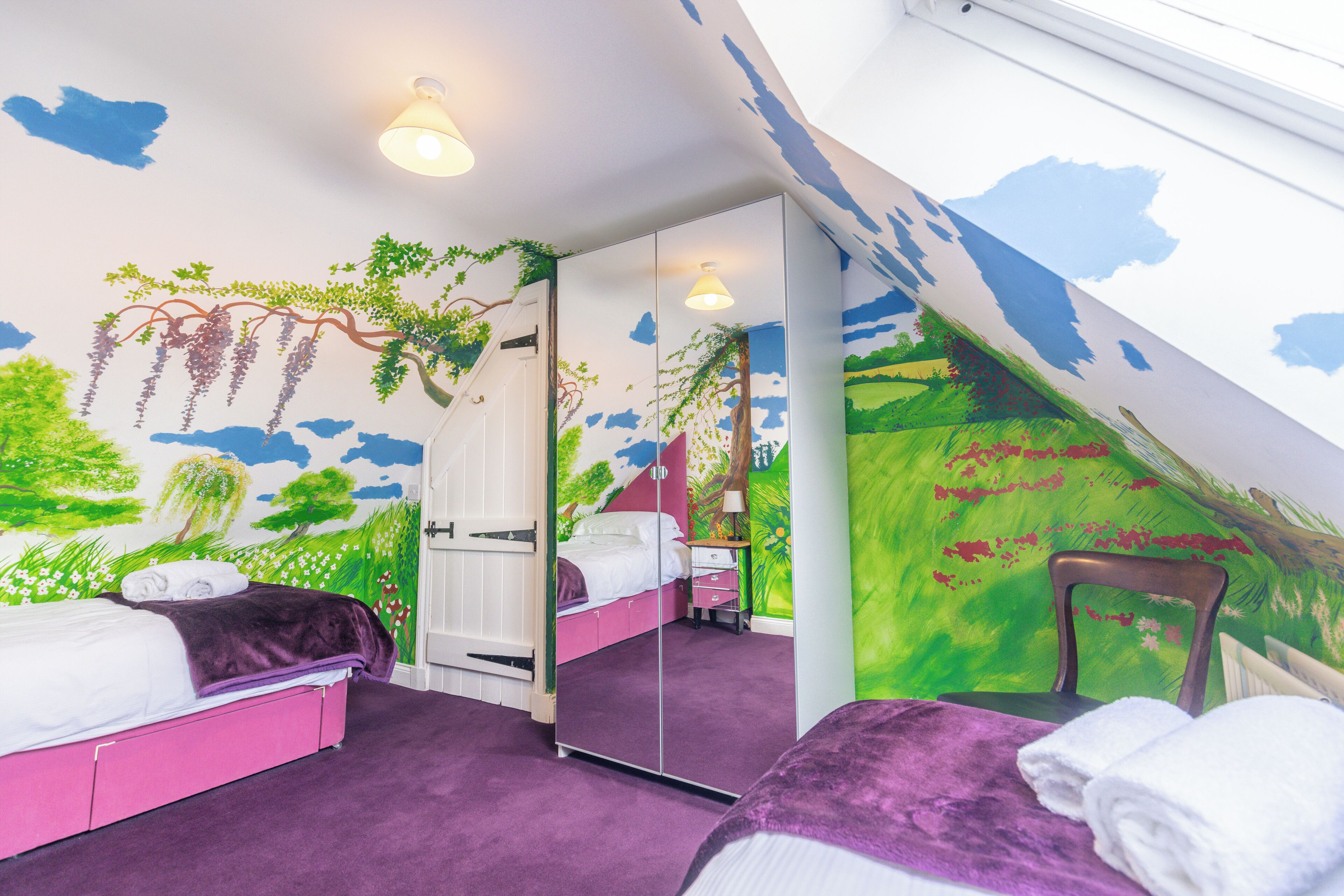 Une chambre avec un tapis violet, un lit avec une literie blanche, une chaise et un miroir.
