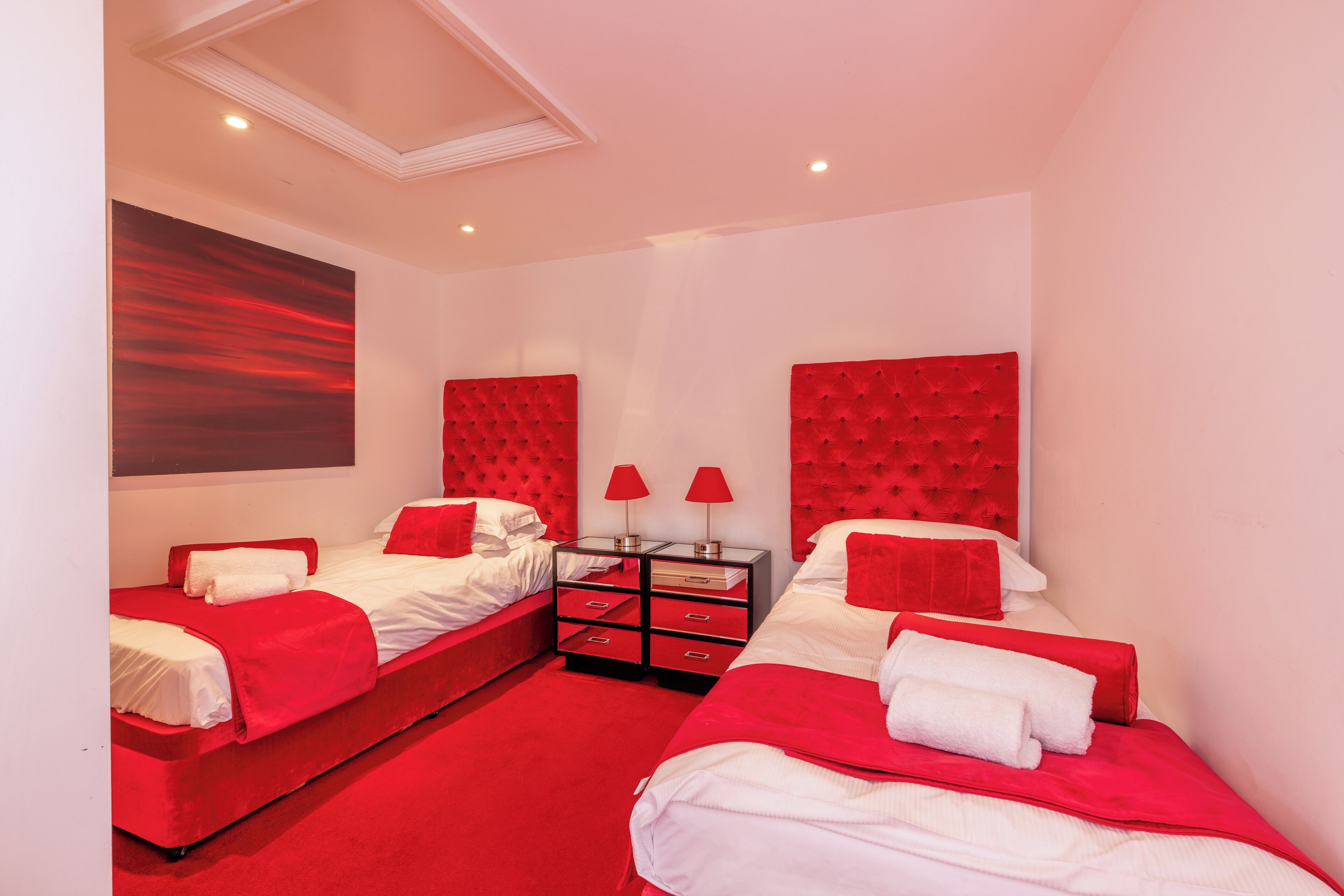 A hotel room with two beds, each with red headboards and white bedding, and a red carpet.