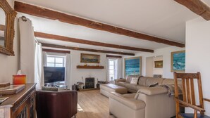 A spacious living room with a wooden ceiling, a large sofa, a wooden chair, and a fireplace. - Budle Newton - North East Escapes (Bamburgh)