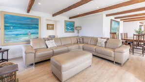 A spacious living room with a large L-shaped beige leather sofa, wooden beams on the ceiling, and a dining area with a wooden table and chairs. - Budle Newton - North East Escapes (Bamburgh)