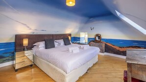 A bedroom with a large bed, wooden floor, a nightstand, a lamp, and a mural of the ocean on the wall. - Budle Newton - North East Escapes (Bamburgh)