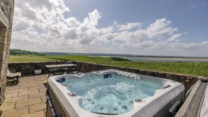A hot tub with a stone wall and a view of a beach and green fields. - Budle Newton - North East Escapes (Bamburgh)