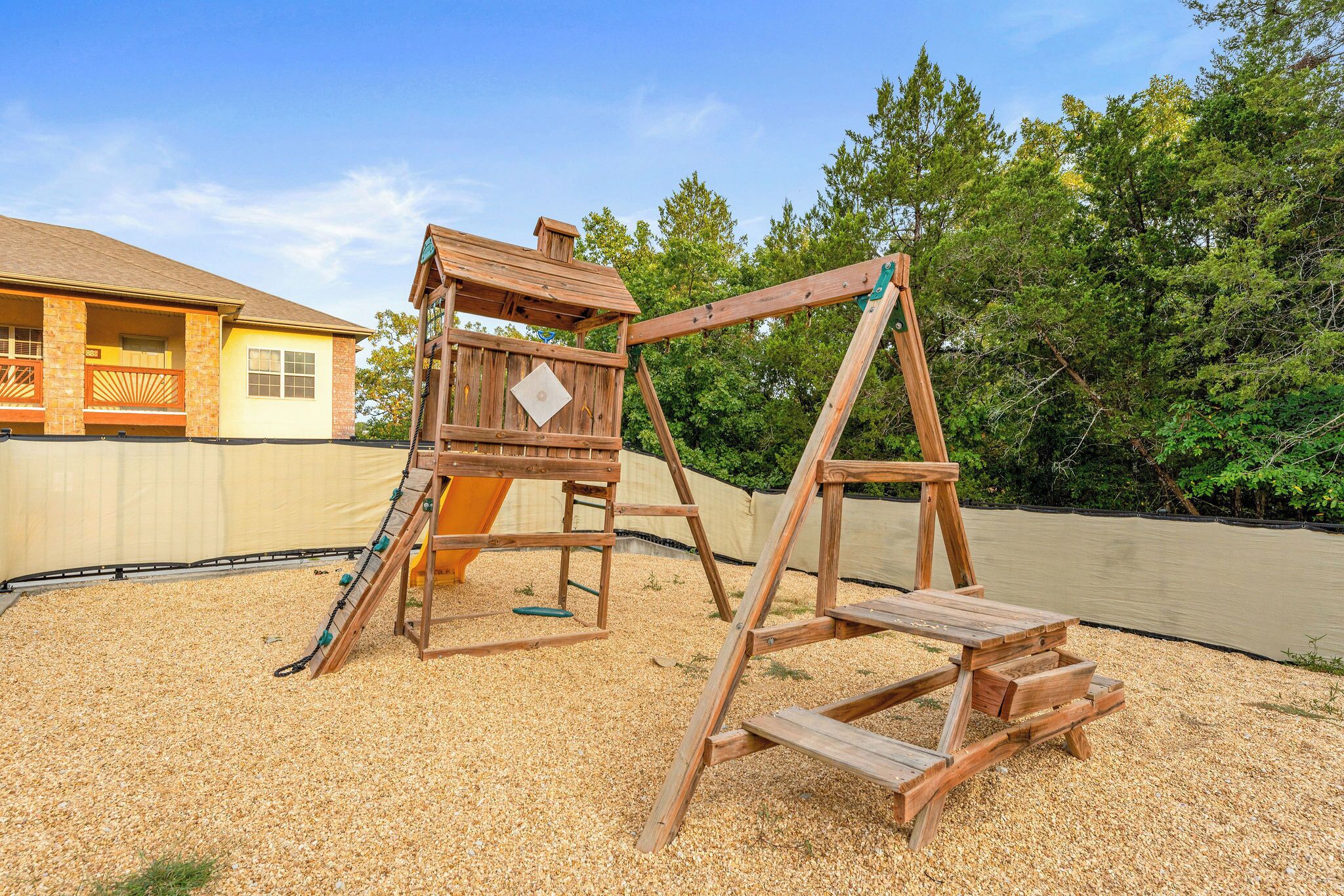 A wooden swing set and slide in a backyard with a house in the background.