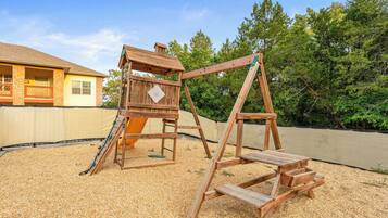 A wooden swing set and slide in a backyard with a house in the background.