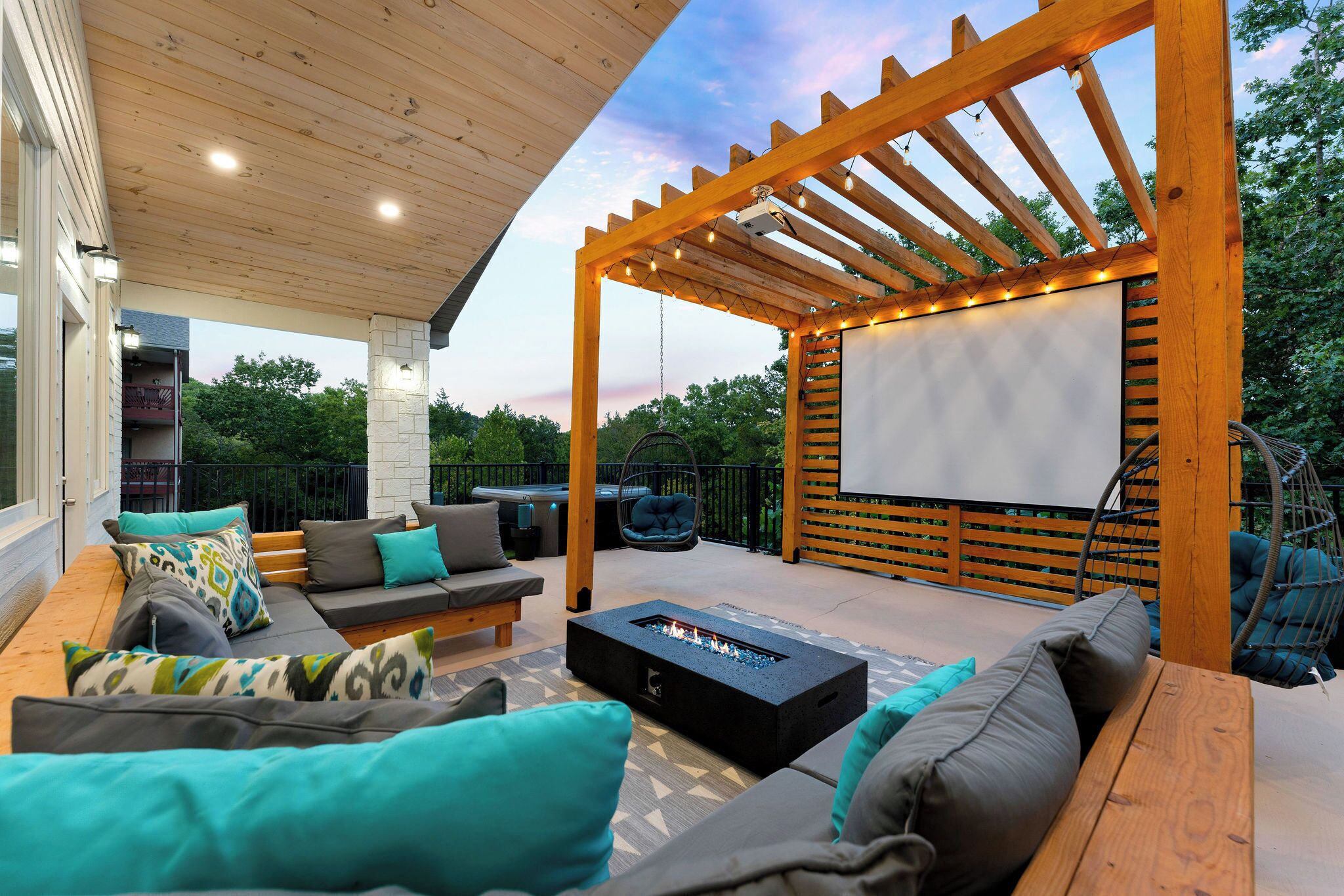 Une terrasse extérieure dotée d’une pergola en bois, d’un espace salon, d’un foyer et d’un grand écran pour les projections de films en plein air.