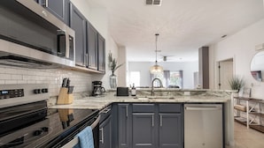 A modern kitchen with dark cabinets, a marble countertop, a built-in oven, and a dishwasher.