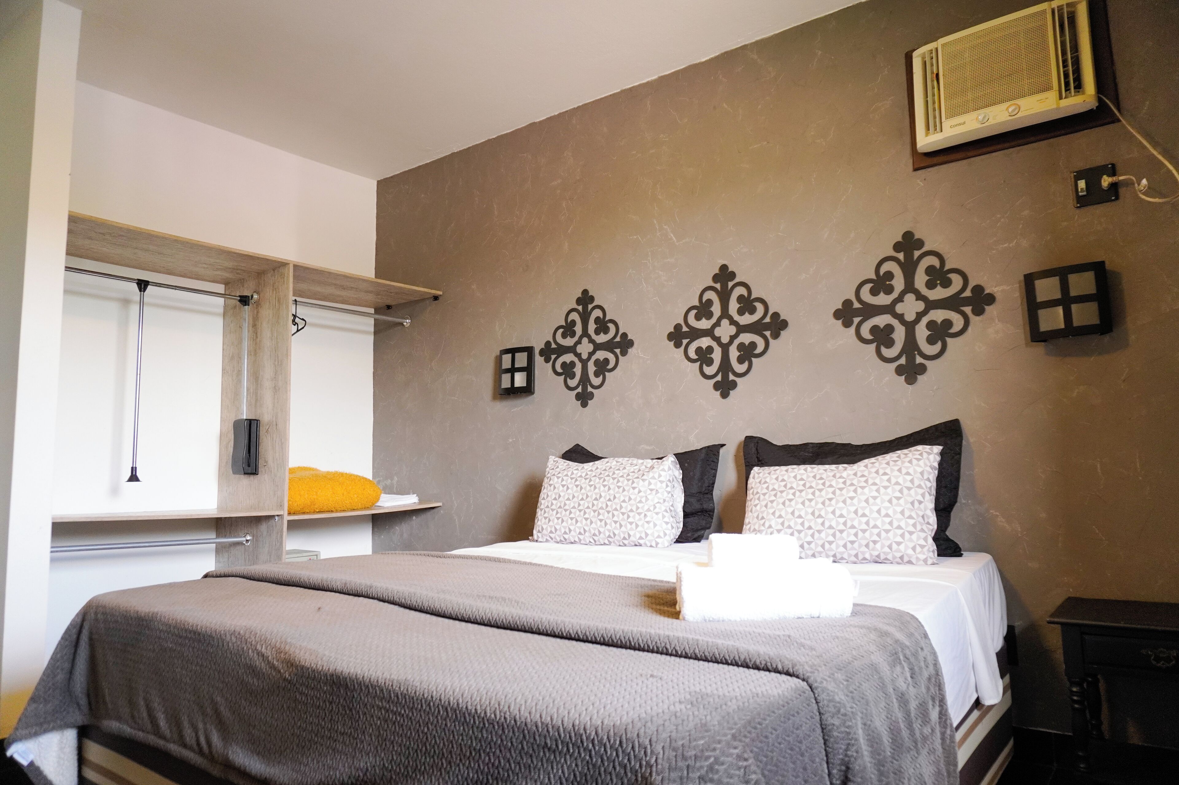 A bedroom with a bed, a window with blinds, a wall-mounted air conditioner, and decorative wall art.
