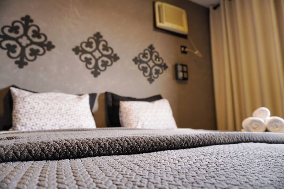 Ein ordentlich bezogenes Bett mit einer gemusterten Decke, eine Wand mit dekorativen Mustern und eine Reihe zusammengerollter Handtücher an der Seite.