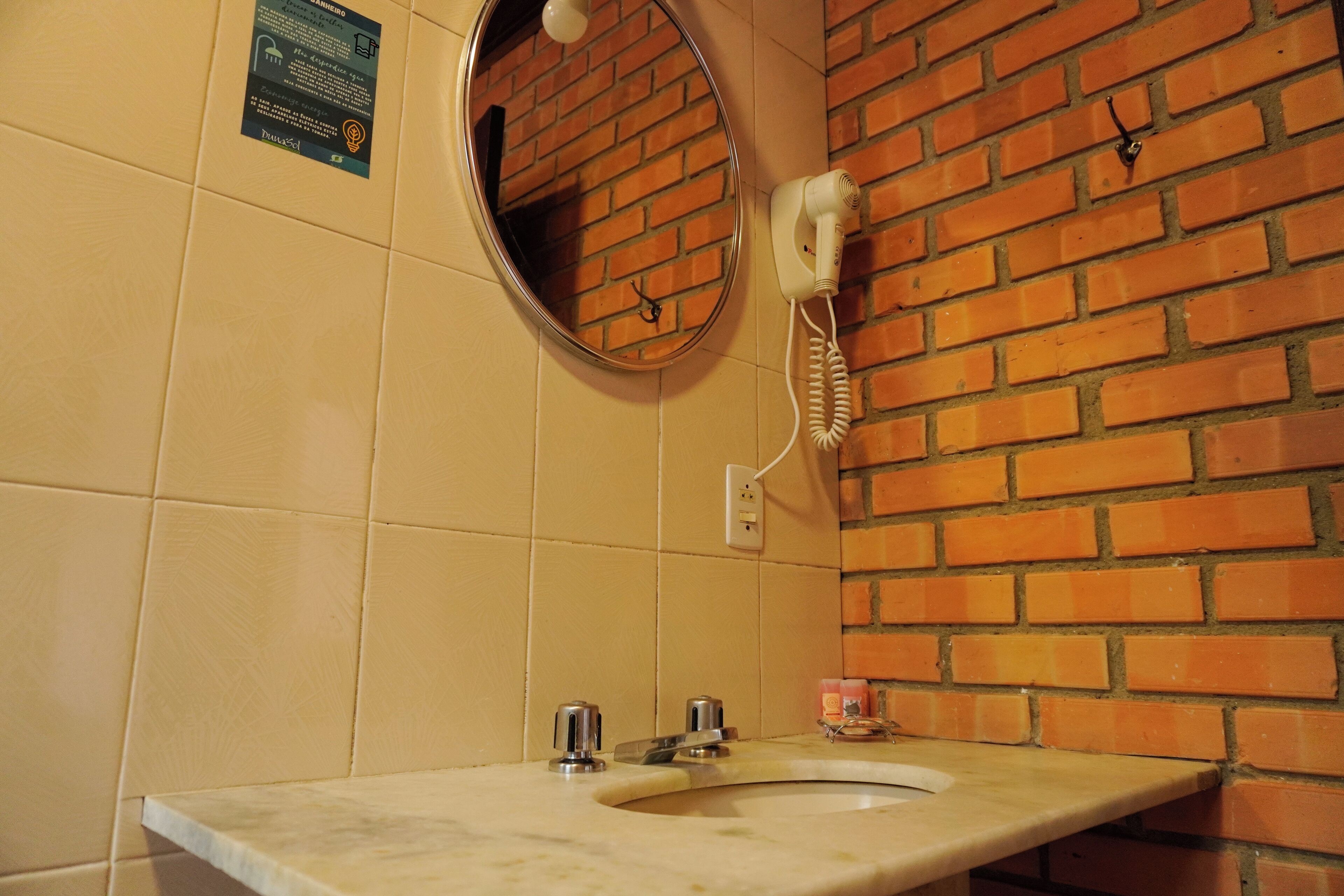 A bathroom with a sink, a mirror, a hairdryer, and a brick wall.