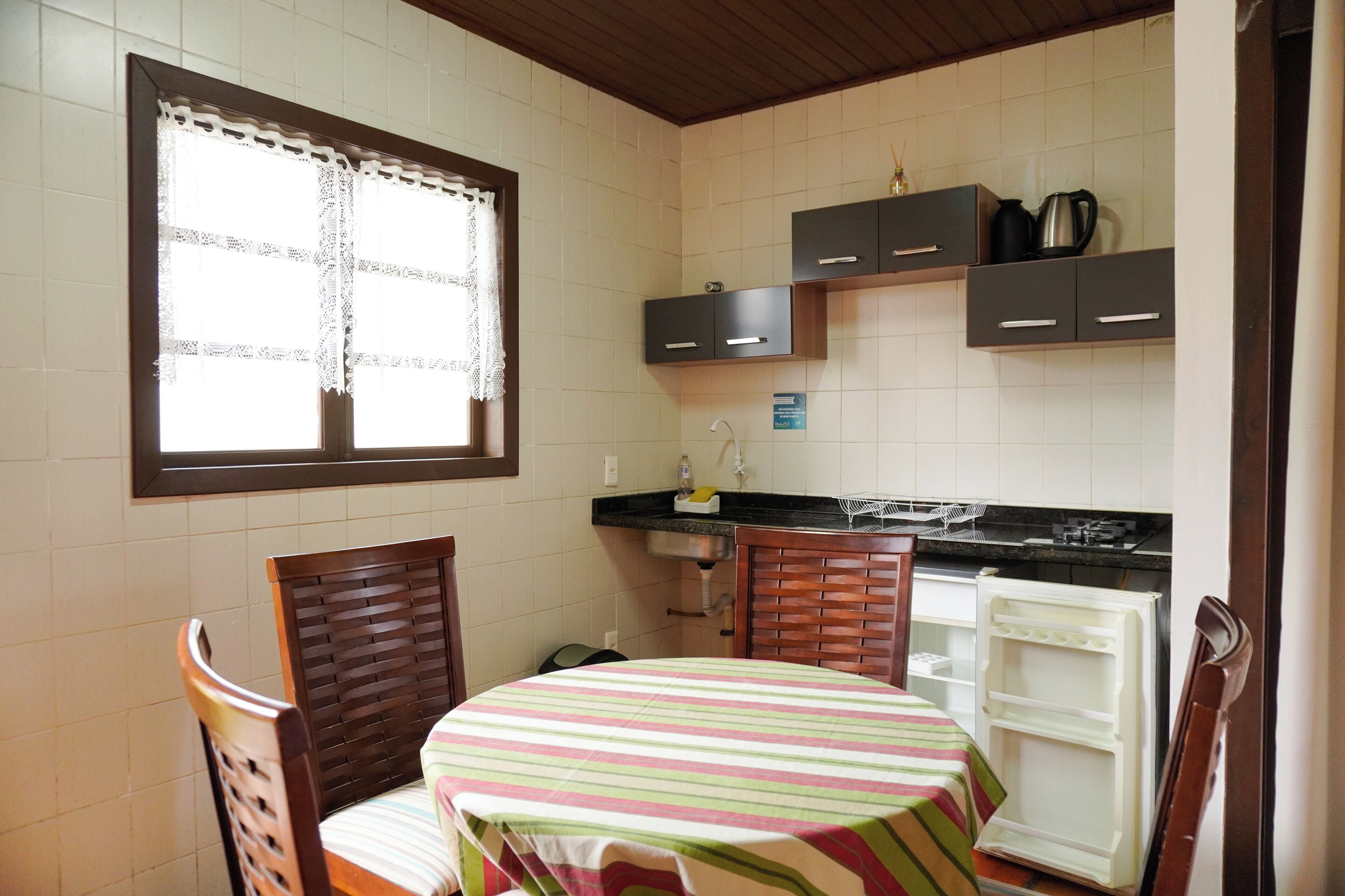 A compact kitchen with a dining table, chairs, a refrigerator, and cabinets.