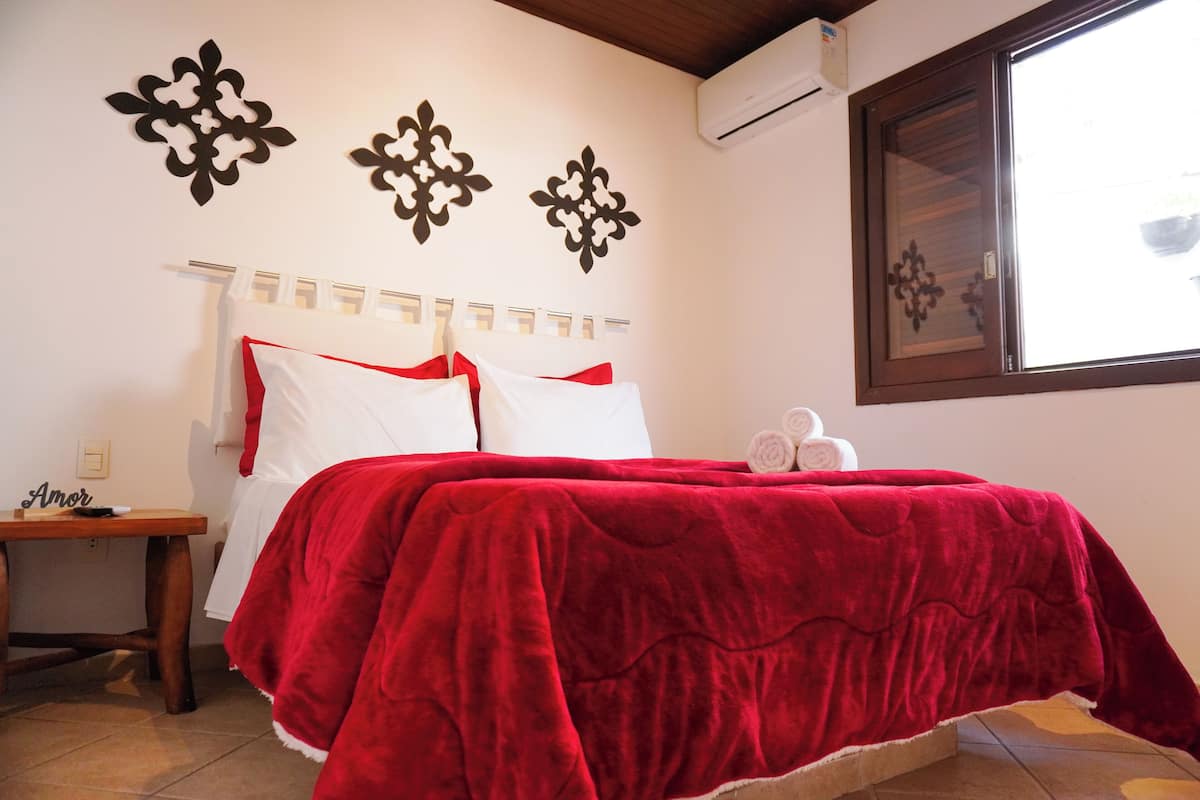Ein Schlafzimmer mit roter Bettdecke, einem hölzernen Nachttisch und Wanddekoration.