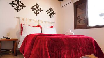 A bedroom with a red bedspread, a wooden nightstand, and decorative wall art.
