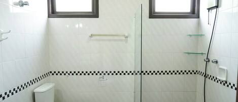 A bathroom with a toilet, a shower, and two windows.
