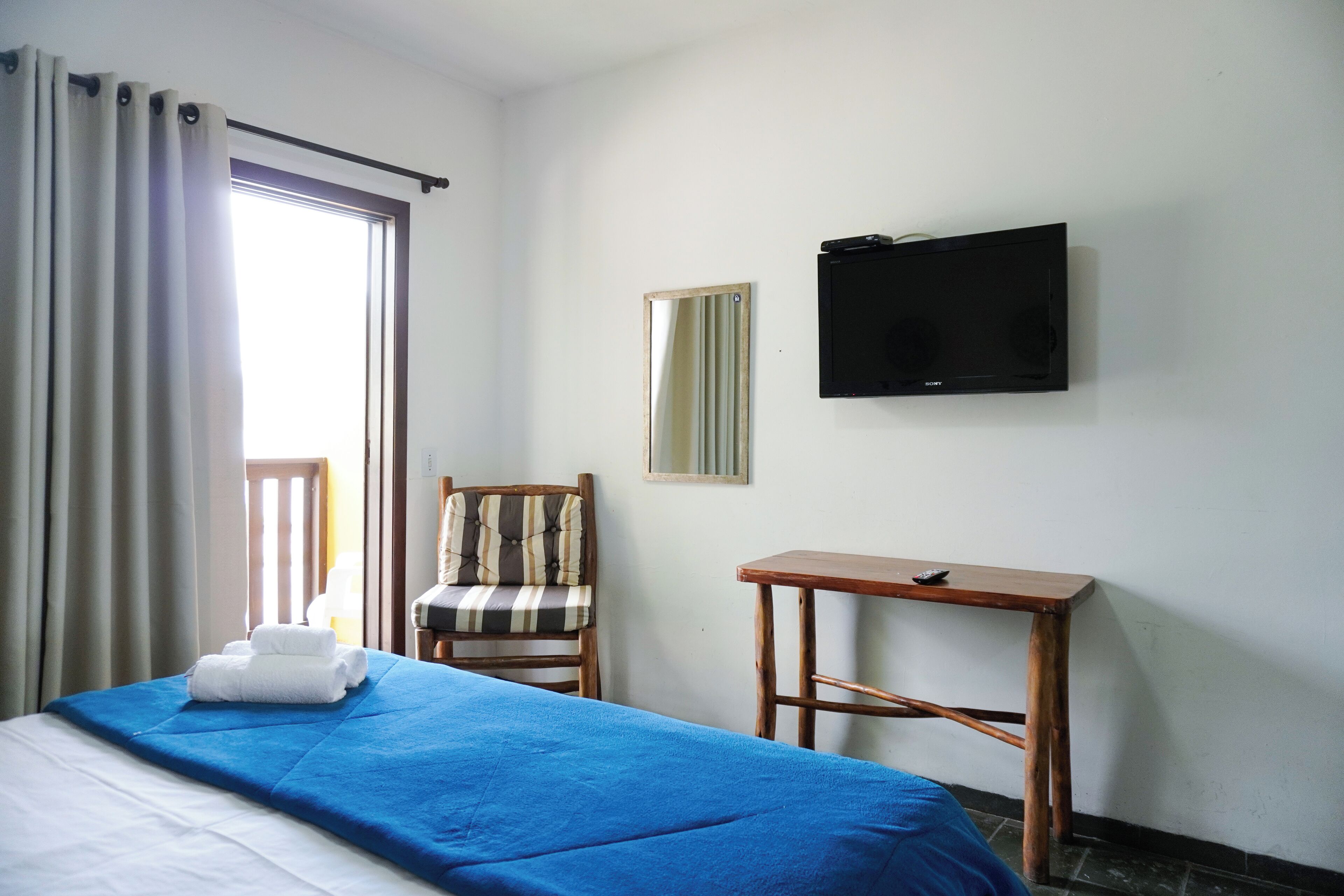 Een hotelkamer met een bed, een stoel, een klein tafeltje, een televisie en een raam met gordijnen.