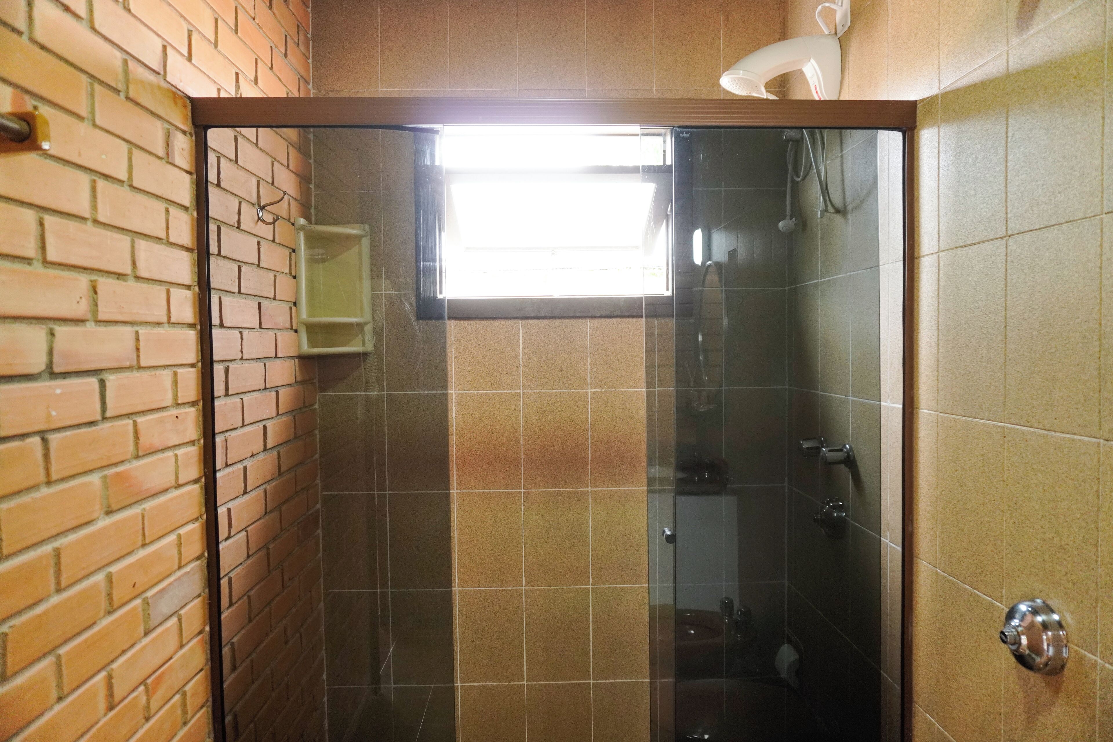 Une salle de bain avec une douche à parois de verre, une fenêtre visible et un mur en briques.